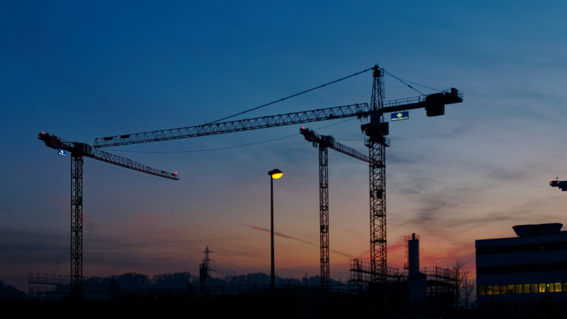 Tower cranes silhouetted over a construction site at dusk