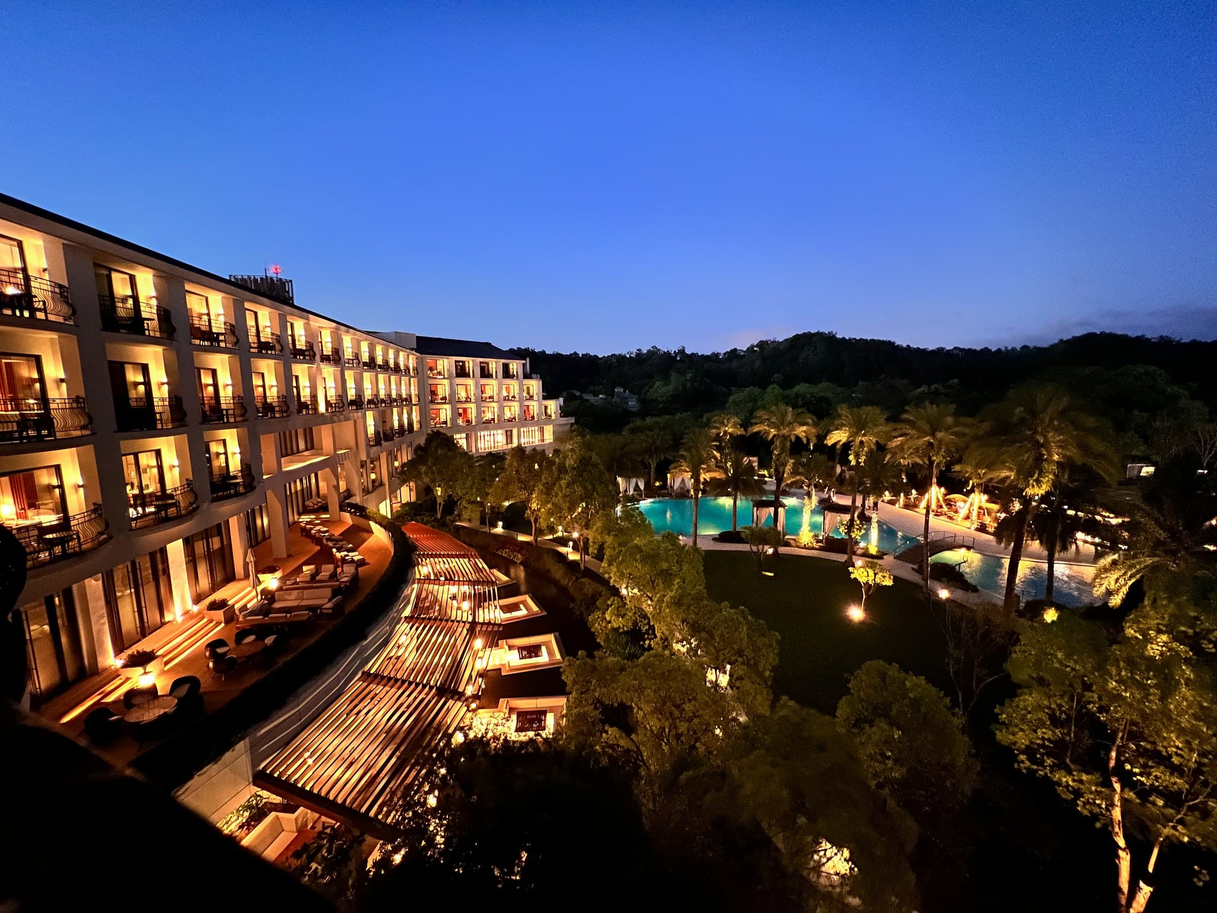 Terraced hotel lit at dusk above its gardens and pool