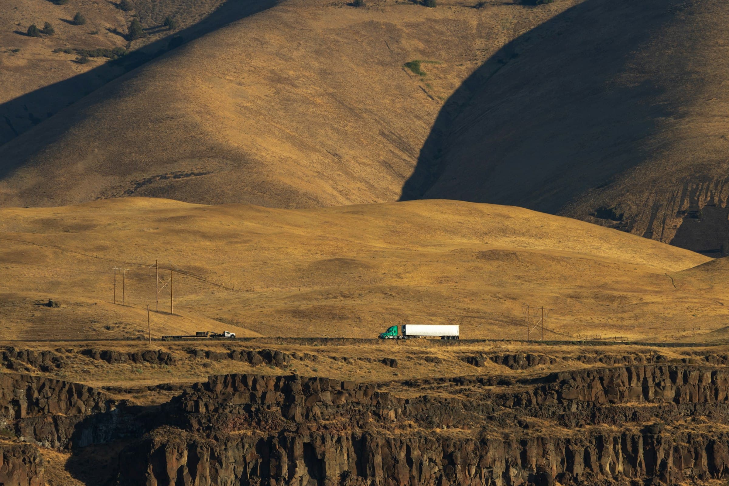 Truck crossing a road below golden hills